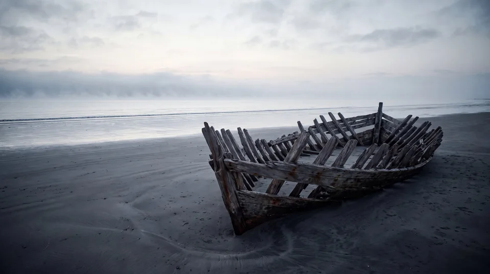 The exposed wooden ribs of a boat resting on a dark beach beneath a cloudy sky — generative artwork.